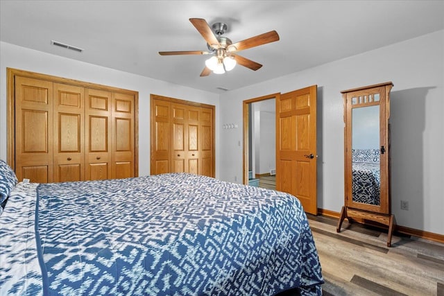 bedroom with visible vents, two closets, baseboards, wood finished floors, and a ceiling fan