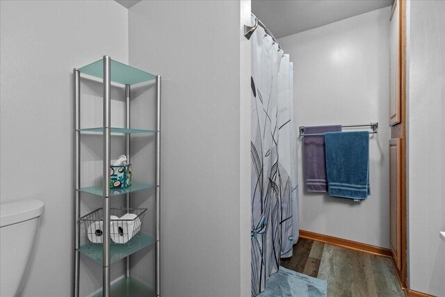 bathroom with a shower with shower curtain, toilet, wood finished floors, and baseboards