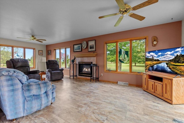 living area with a ceiling fan, a fireplace, visible vents, and baseboards