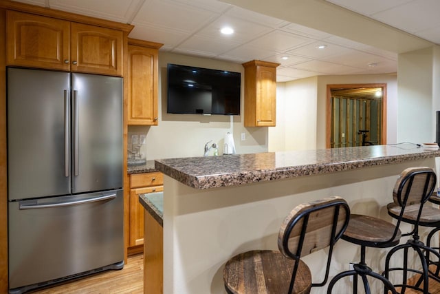 kitchen with light wood-type flooring, kitchen peninsula, stainless steel refrigerator, and a breakfast bar