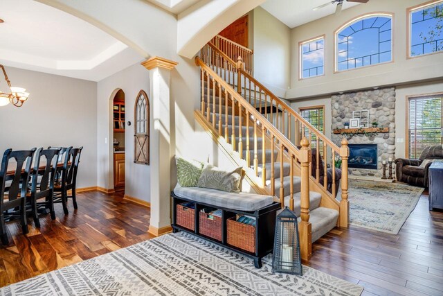 stairway with a towering ceiling, hardwood / wood-style floors, ceiling fan, and a stone fireplace