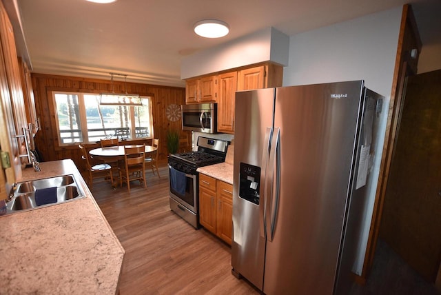 kitchen featuring appliances with stainless steel finishes, hardwood / wood-style flooring, wood walls, and sink