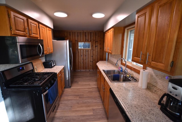 kitchen featuring wooden walls, light hardwood / wood-style flooring, light stone countertops, stainless steel appliances, and sink