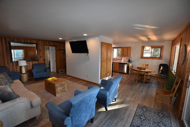 living room with a wealth of natural light, sink, wood-type flooring, and wooden walls