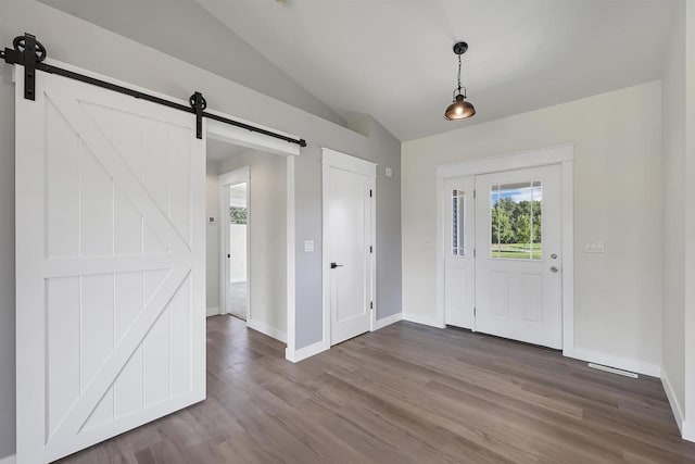 foyer with a barn door, wood-type flooring, a wealth of natural light, and vaulted ceiling