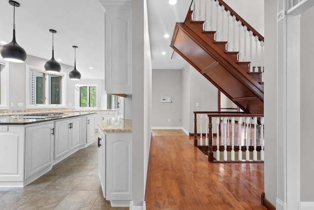 kitchen featuring light wood-type flooring, white cabinetry, stainless steel gas stovetop, light stone countertops, and hanging light fixtures