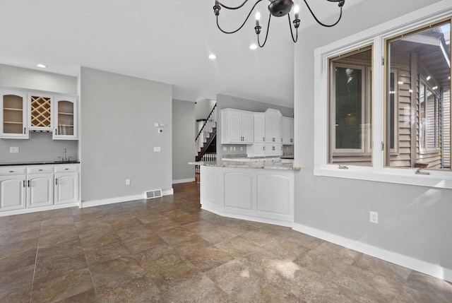 interior space with an inviting chandelier, sink, light stone countertops, and white cabinets