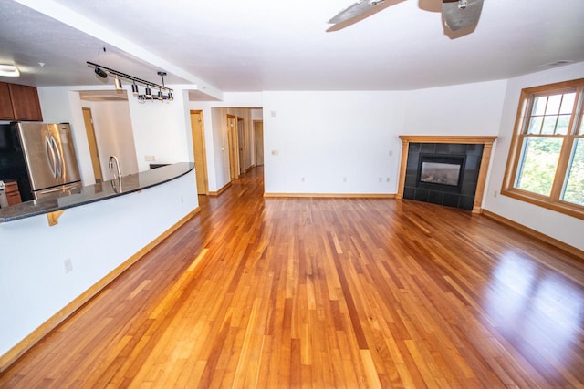 unfurnished living room with ceiling fan, a tiled fireplace, light hardwood / wood-style floors, and sink