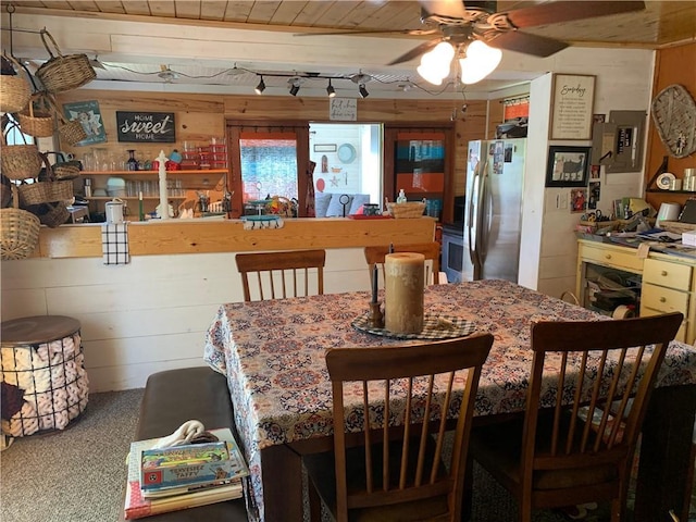 carpeted dining space featuring ceiling fan and wooden walls