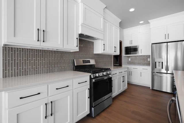 kitchen with white cabinets, stainless steel appliances, premium range hood, dark hardwood / wood-style floors, and tasteful backsplash