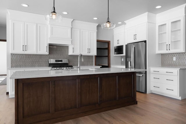 kitchen with a kitchen island with sink, light hardwood / wood-style flooring, decorative light fixtures, and stainless steel appliances