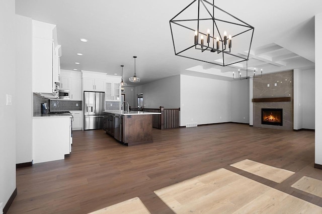 kitchen with stainless steel appliances, an inviting chandelier, hanging light fixtures, dark wood-type flooring, and a center island with sink