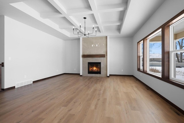 unfurnished living room with light wood-type flooring, coffered ceiling, a chandelier, a tile fireplace, and beam ceiling