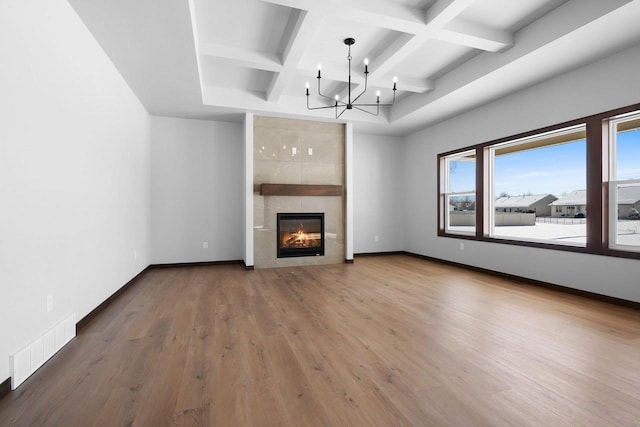 unfurnished living room featuring a tiled fireplace, coffered ceiling, hardwood / wood-style flooring, and a notable chandelier