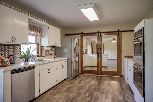 kitchen featuring white cabinets, a barn door, appliances with stainless steel finishes, sink, and dark wood-type flooring