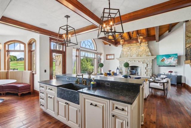 kitchen with dark hardwood / wood-style floors, a fireplace, a center island with sink, hanging light fixtures, and a chandelier