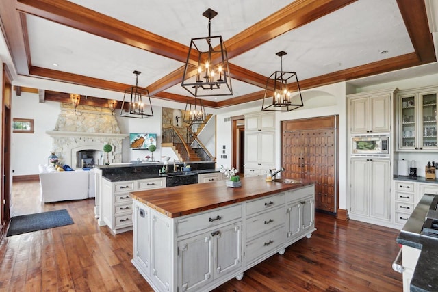 kitchen with a fireplace, decorative light fixtures, dark hardwood / wood-style flooring, butcher block countertops, and a center island with sink