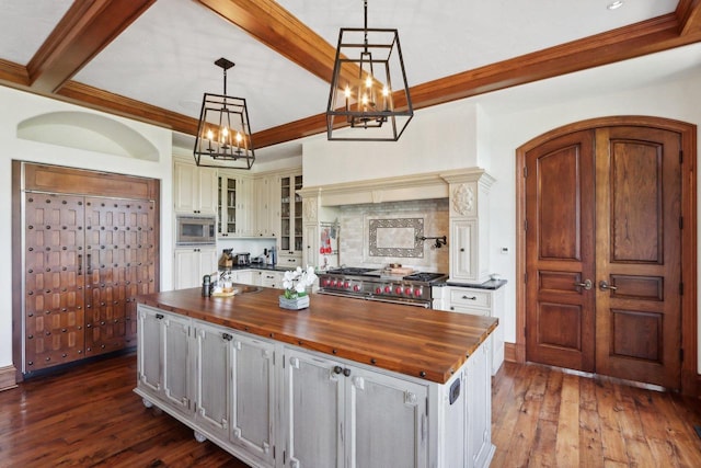 kitchen featuring butcher block countertops, dark hardwood / wood-style flooring, pendant lighting, stainless steel appliances, and a large island with sink