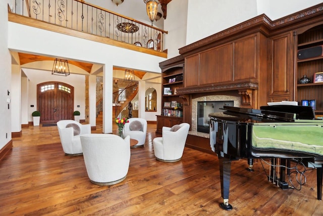 living room with a notable chandelier, wood-type flooring, a towering ceiling, and a fireplace