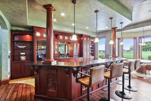 bar with light hardwood / wood-style floors, built in shelves, decorative columns, and hanging light fixtures