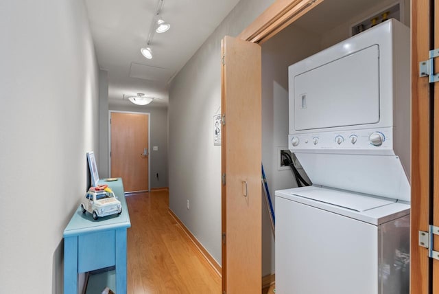 clothes washing area featuring stacked washer and dryer, rail lighting, light wood finished floors, baseboards, and laundry area