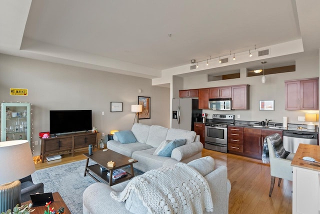 living area featuring a tray ceiling, light wood-style floors, and visible vents