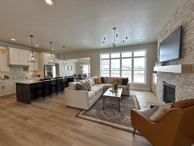 living room featuring recessed lighting, a stone fireplace, light wood finished floors, and an inviting chandelier