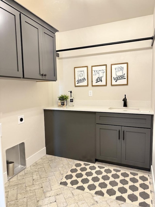 washroom featuring brick floor, hookup for an electric dryer, a sink, baseboards, and cabinet space