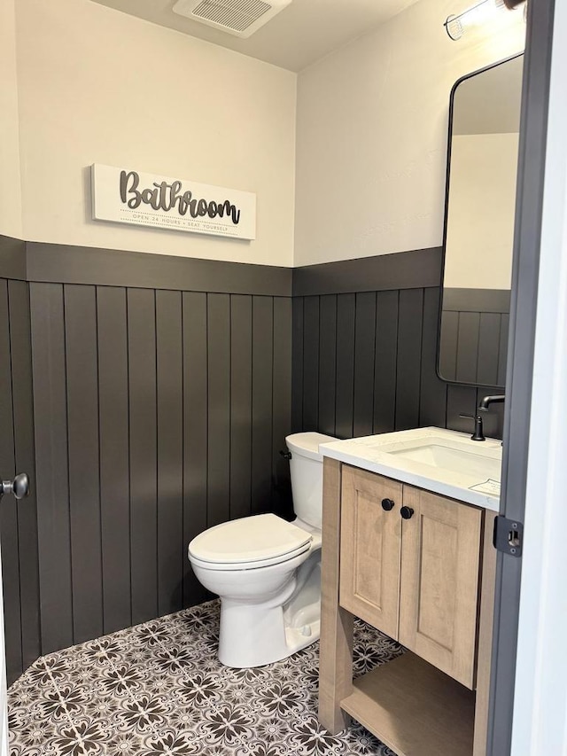 bathroom with tile patterned flooring, toilet, a wainscoted wall, visible vents, and vanity