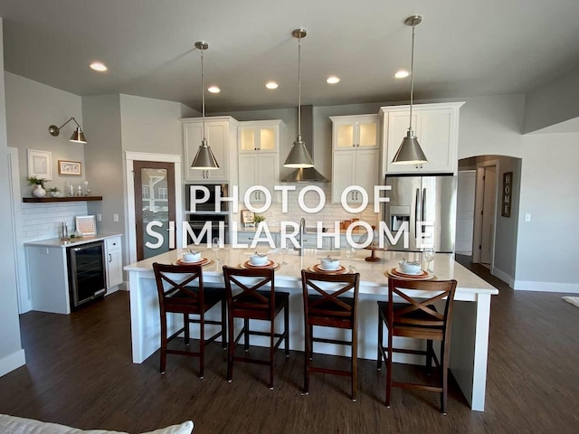 kitchen with stainless steel fridge, pendant lighting, light countertops, and a kitchen island with sink