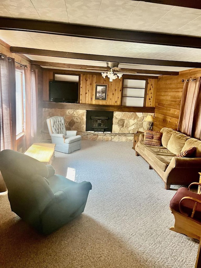 carpeted living room featuring wood walls, ceiling fan, a fireplace, and beamed ceiling