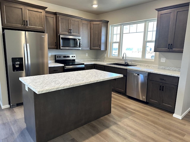 kitchen with sink, light hardwood / wood-style flooring, appliances with stainless steel finishes, dark brown cabinets, and a kitchen island