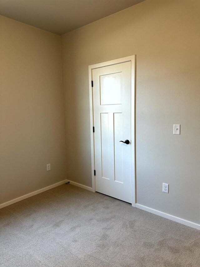 spare room featuring light carpet and baseboards