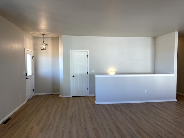 empty room with visible vents, baseboards, wood finished floors, and a chandelier