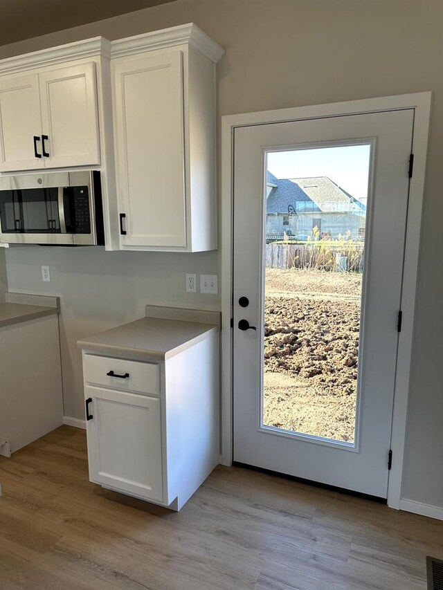 kitchen featuring stainless steel microwave, a healthy amount of sunlight, light wood-style flooring, and white cabinetry