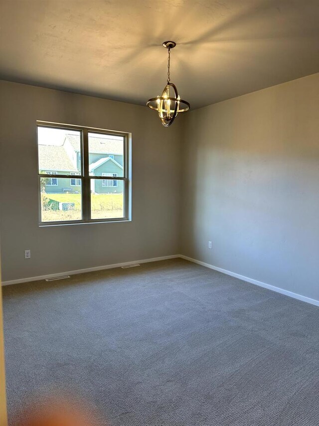 unfurnished room featuring a chandelier, visible vents, dark carpet, and baseboards