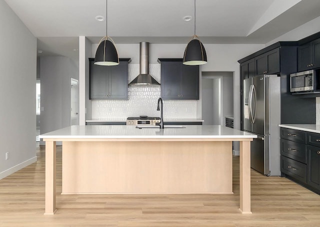 kitchen featuring sink, stainless steel appliances, wall chimney range hood, a kitchen breakfast bar, and a center island with sink