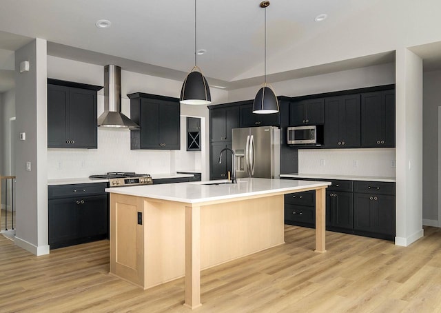 kitchen featuring sink, wall chimney exhaust hood, stainless steel appliances, light hardwood / wood-style floors, and a center island with sink