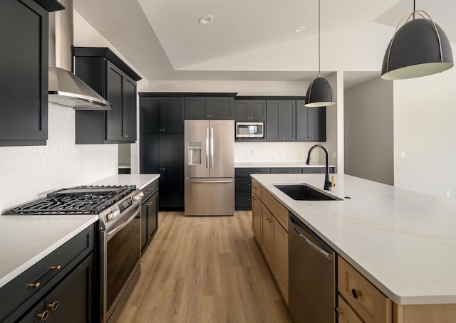 kitchen with appliances with stainless steel finishes, vaulted ceiling, sink, wall chimney range hood, and light hardwood / wood-style flooring