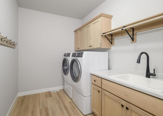 laundry area featuring washer and dryer, light hardwood / wood-style flooring, cabinets, and sink