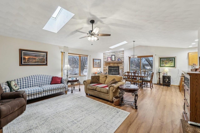 living room with a stone fireplace, vaulted ceiling with skylight, light wood-type flooring, and ceiling fan