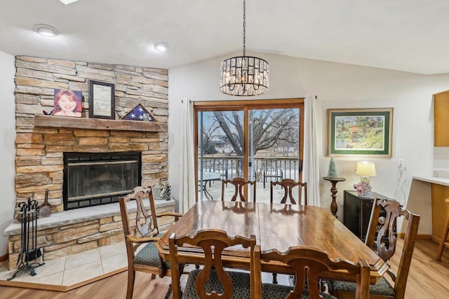 dining room with a stone fireplace, vaulted ceiling, light wood-type flooring, and a chandelier