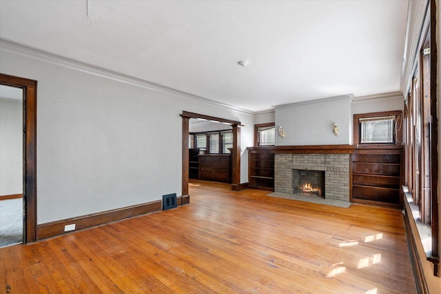 unfurnished living room featuring visible vents, crown molding, baseboards, a fireplace, and wood-type flooring