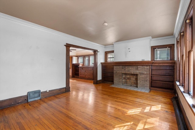 unfurnished living room with visible vents, hardwood / wood-style flooring, a fireplace, crown molding, and ornate columns