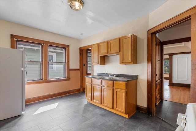 kitchen featuring dark countertops, freestanding refrigerator, baseboards, and a sink