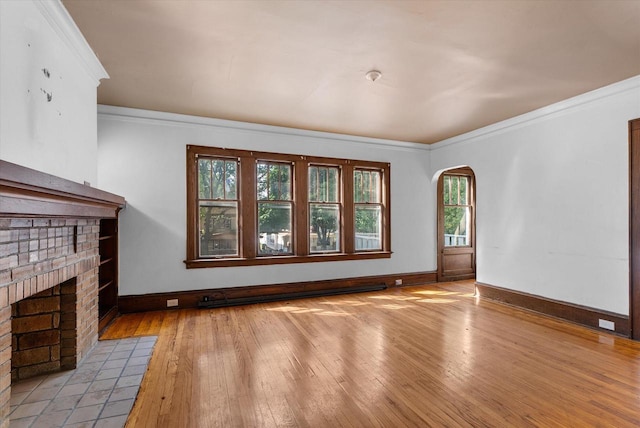 unfurnished living room with light wood-type flooring, a fireplace, crown molding, and a healthy amount of sunlight