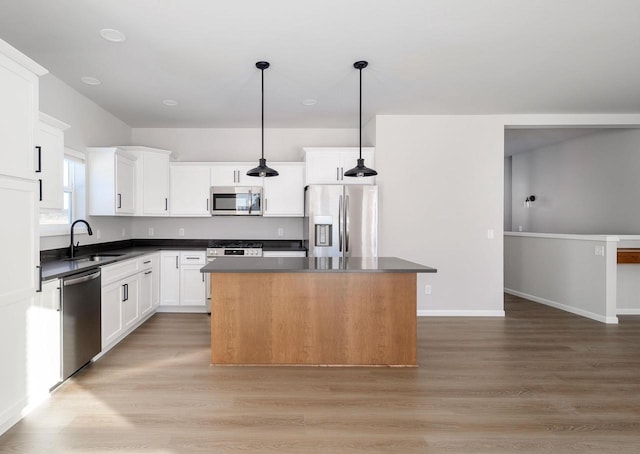 kitchen featuring white cabinetry, a center island, sink, stainless steel appliances, and decorative light fixtures