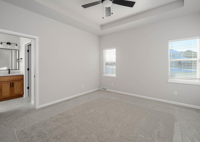 carpeted spare room with ceiling fan, a raised ceiling, and sink