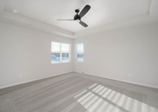 carpeted empty room with ceiling fan and a tray ceiling