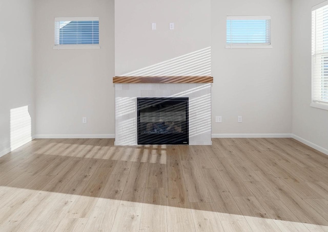 unfurnished living room with light hardwood / wood-style floors, a wealth of natural light, and a tiled fireplace